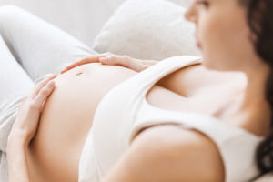 Waiting for a baby. Close-up of pregnant young woman in white tank top touching her belly